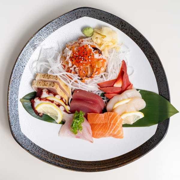 Assorted sashimi platter with tuna, salmon, scallops, octopus, and roe on a white plate.