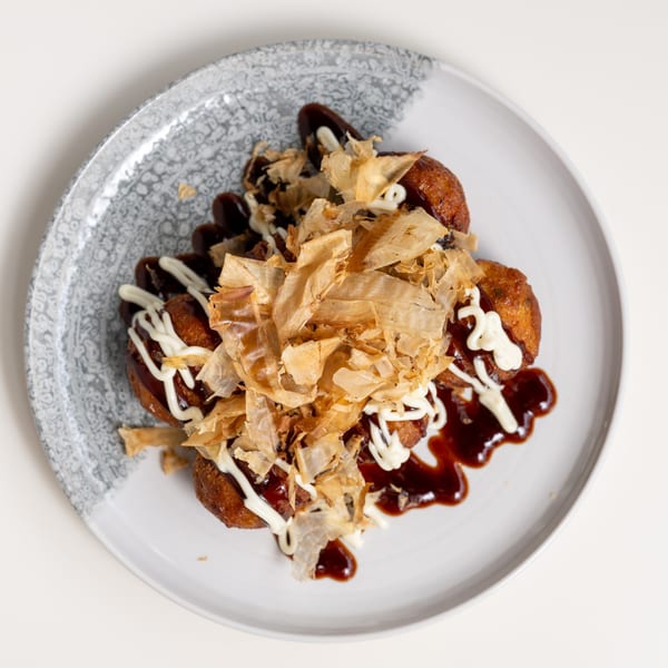 Japanese takoyaki, drizzled with sauce and mayonnaise, topped with bonito flakes on a white plate.