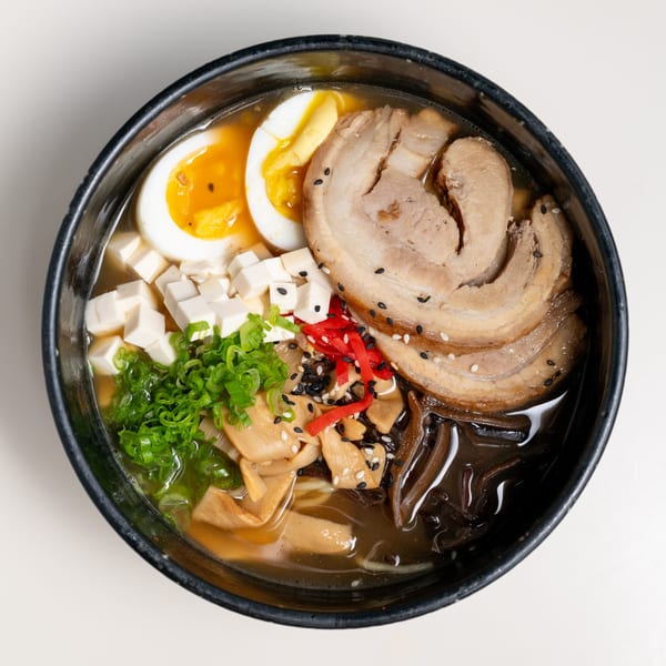 A black bowl of Seiko Japanese Restaurant's ramen with pork, egg, tofu, and green onions.